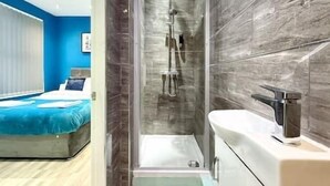 Un baño moderno con ducha envuelta en vidrio, lavamanos blanco y pared con azulejos de mármol.