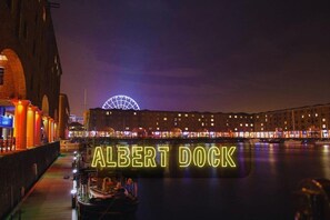A nighttime view of the Albert Dock with illuminated signage and a distinctive arch structure in the background. - Liverpool Serviced Apartment | Mallow (Liverpool)