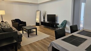 Una sala de estar moderna con un sofá, sillas, una mesa de centro, un televisor y un comedor con una mesa y sillas.