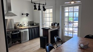 A modern kitchen with a wooden dining table, black chairs, and a view of the outdoors through large windows. - Charming house with panoramic terrace in Domme - Sarlat (Domme)