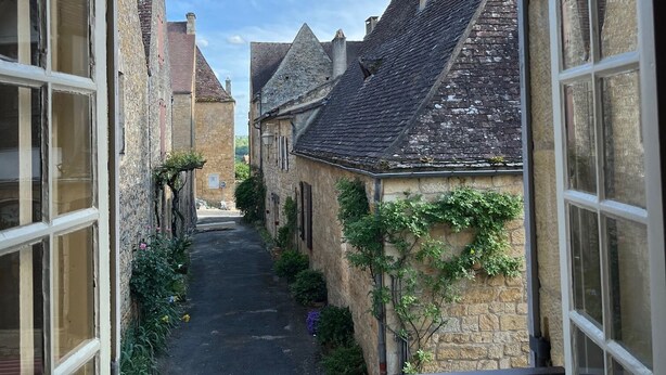 A narrow street with stone buildings, a clear sky, and a view through an open window. - Charming house with panoramic terrace in Domme - Sarlat (Domme)