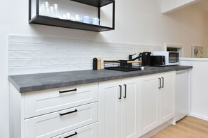 A kitchen with white cabinets, a grey countertop, a microwave, a coffee maker, and a shelf with cups and glasses. - Kookaburras Family Retreat in Nelson Bay (Nelson Bay)