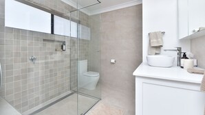 A modern bathroom with a glass-enclosed shower, a toilet, and a vanity with a sink and towel rack. - Kookaburras Holiday House with Pool in Nelson Bay (Nelson Bay)
