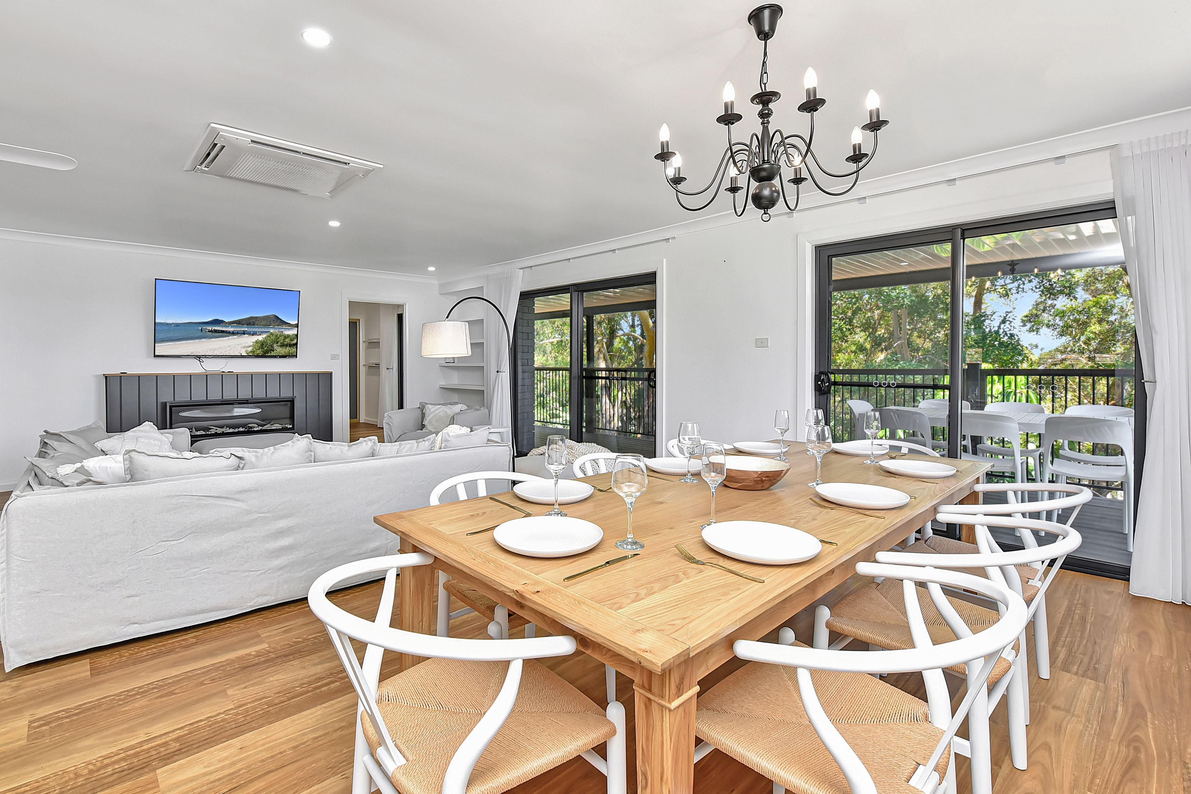 A modern dining room with a wooden table set for six, white chairs, and a chandelier.