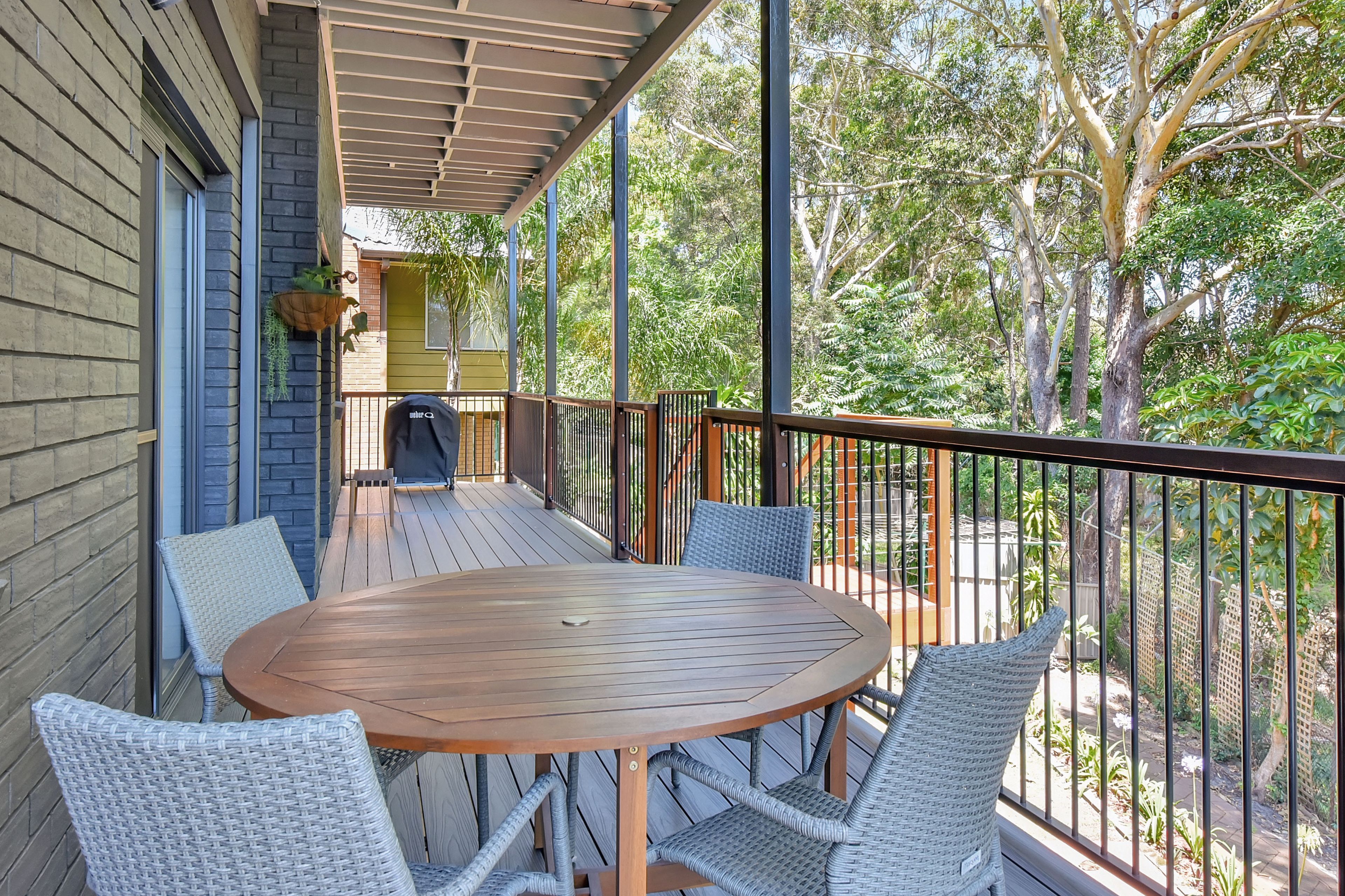 A covered outdoor patio with a round wooden table and wicker chairs.