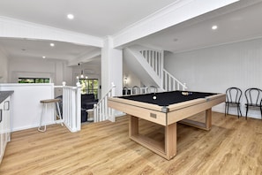 A pool table in a room with wooden flooring, white walls, and a staircase. - Kookaburras (Nelson Bay)