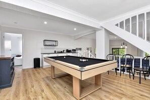 A modern living room with a pool table, a dining area with chairs, and a staircase. - Kookaburras Family Retreat in Nelson Bay (Nelson Bay)