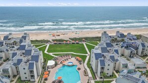 Un hotel frente a la playa con piscina, sombrillas y vista al océano.