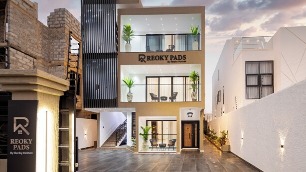 A modern building with a sign for "Recky Pads by Recky Homes" and a staircase leading to an upper level. - Reoky Pads - Redefining comfort and luxury. (Accra)