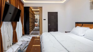 A modern hotel room with a large bed, a flat-screen TV mounted on the wall, and a walk-in closet with shelves. - Reoky Pads - Redefining comfort and luxury. (Accra)