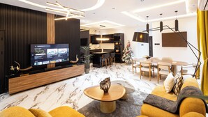 A modern living room with a large TV, comfortable seating, a dining area, and a kitchen in the background. - Reoky Pads - Redefining comfort and luxury. (Accra)
