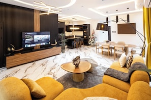 A modern living room with a large TV, comfortable seating, a dining area, and a kitchen in the background. - Reoky Pads - Redefining comfort and luxury. (Accra)
