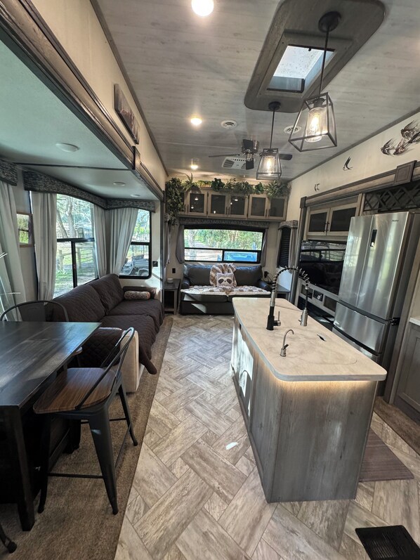 A compact RV kitchen with a central island, built-in cabinets, and a dining area with a sofa and table. - Cozy campground in charming Pierson with AC, WiFi (Pierson)