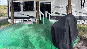 Ein überdachter Außenbereich mit einer grünen Terrasse, einem Grill und einem weißen Wohnmobil mit dem Schriftzug "RESIDENCE".