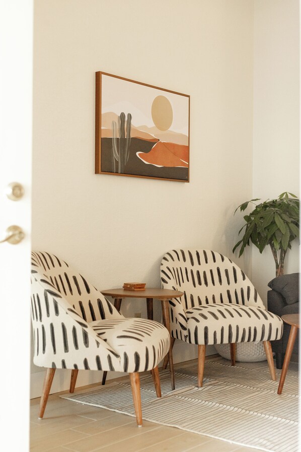 A room with two patterned chairs, a small table, and a framed artwork on the wall.