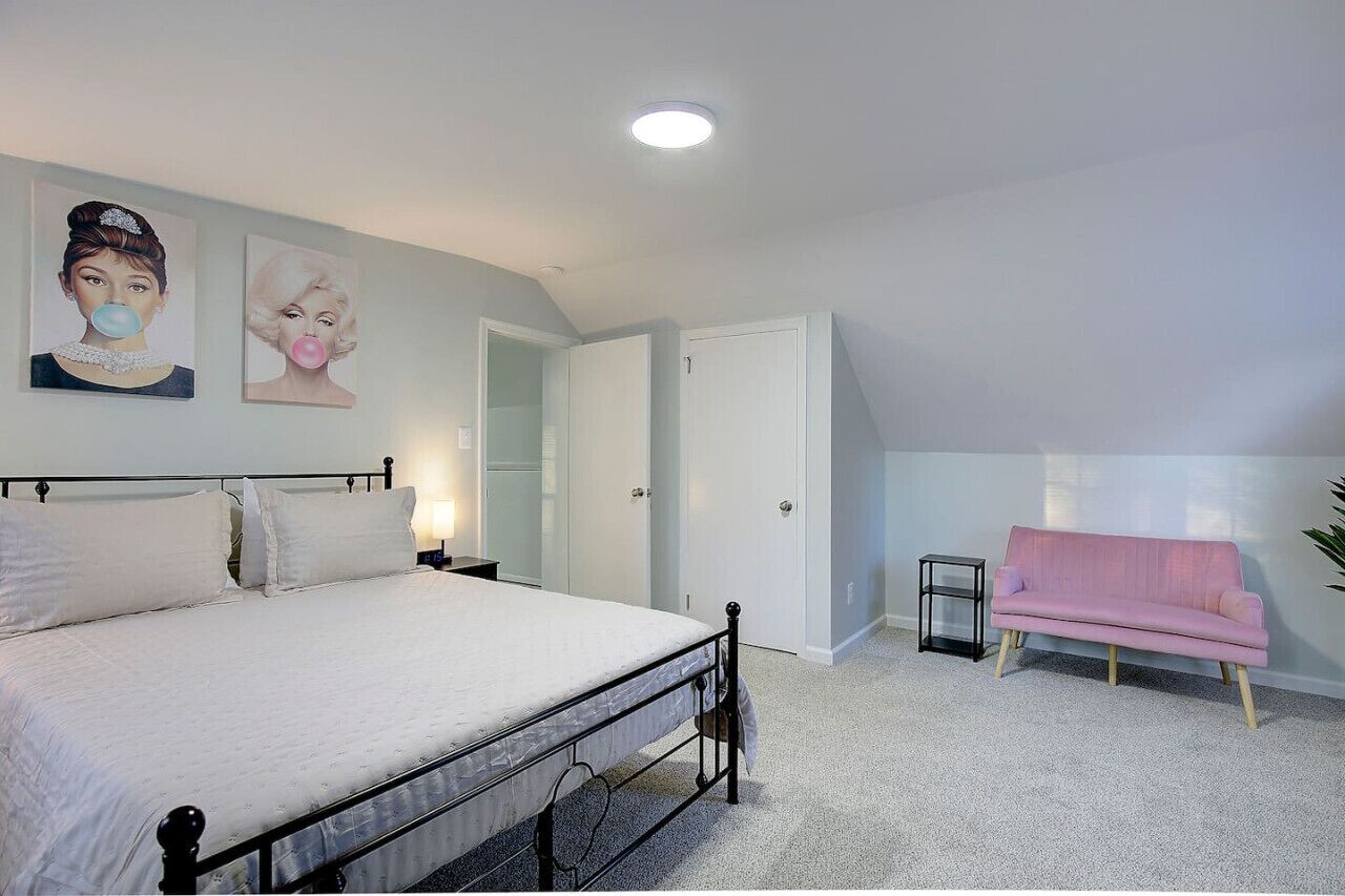 Un dormitorio con una cama, un sofá rosa y dos obras de arte en la pared.