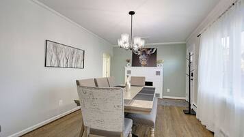 Een eetgedeelte met een houten tafel, stoelen en een kroonluchter. Er is een open haard met een decoratieve schouw en een schilderij aan de muur.
