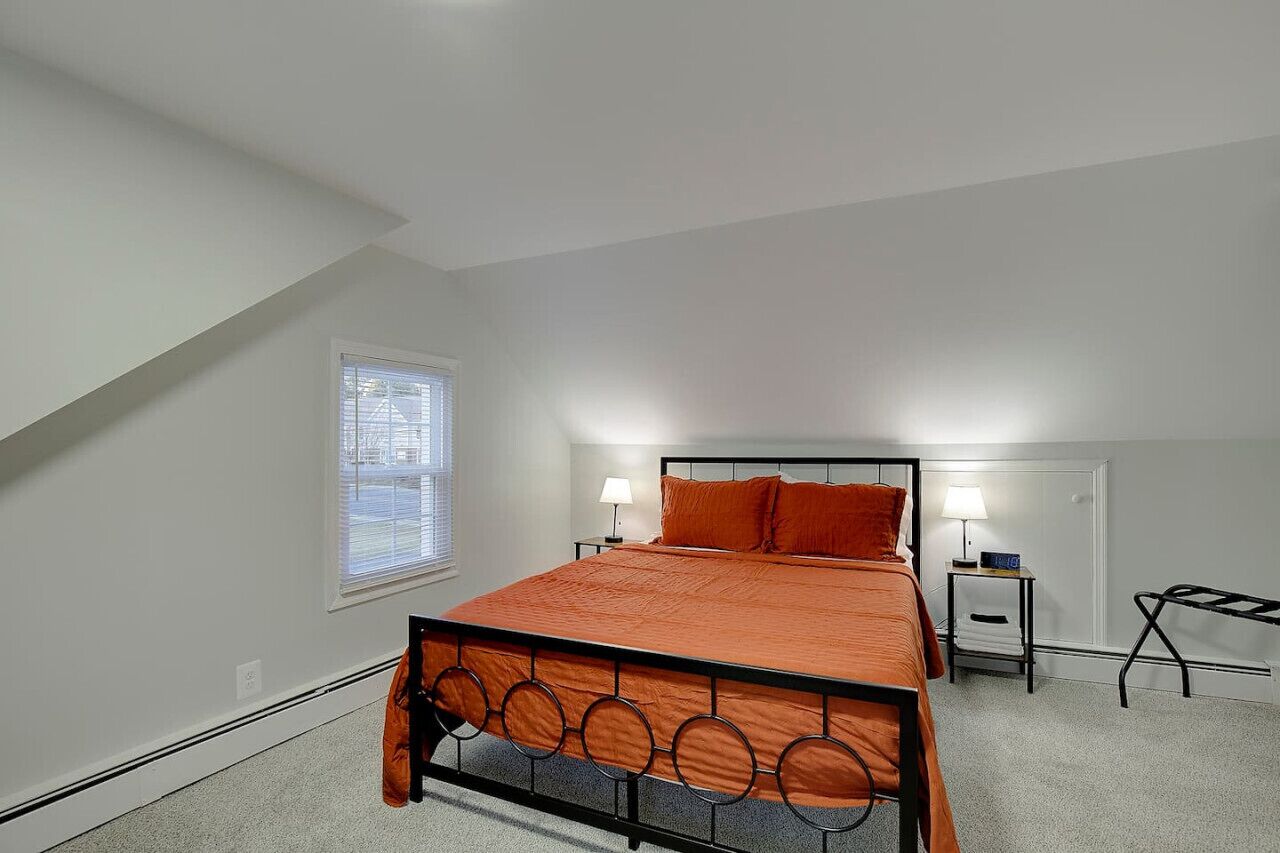 A bedroom with a bed, two bedside tables, a window, and a radiator.