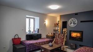A cozy living room with a fireplace, a sofa, a coffee table, and a window with curtains. - 3 Chambres table d'hôtes in the countryside le nid qui danse near Vesoul 8 to 11 pers. (Baignes)