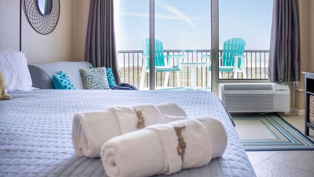 A hotel room with a large bed, a balcony with chairs, and a view of the beach. - 213 Beachfront Heated Pool Gulf View Studio (Galveston)