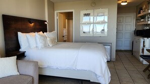 Un dormitorio con cama, mesita de noche, una silla y baño visible a través de una puerta abierta.