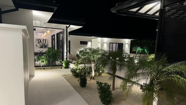 A modern outdoor area with a pathway leading to a building, surrounded by palm trees and a gravel surface. - Villa Gouverneur, Tamarindo, hacienda Pinilla, Avellanas, Langosta, Costa Rica (Tamarindo)