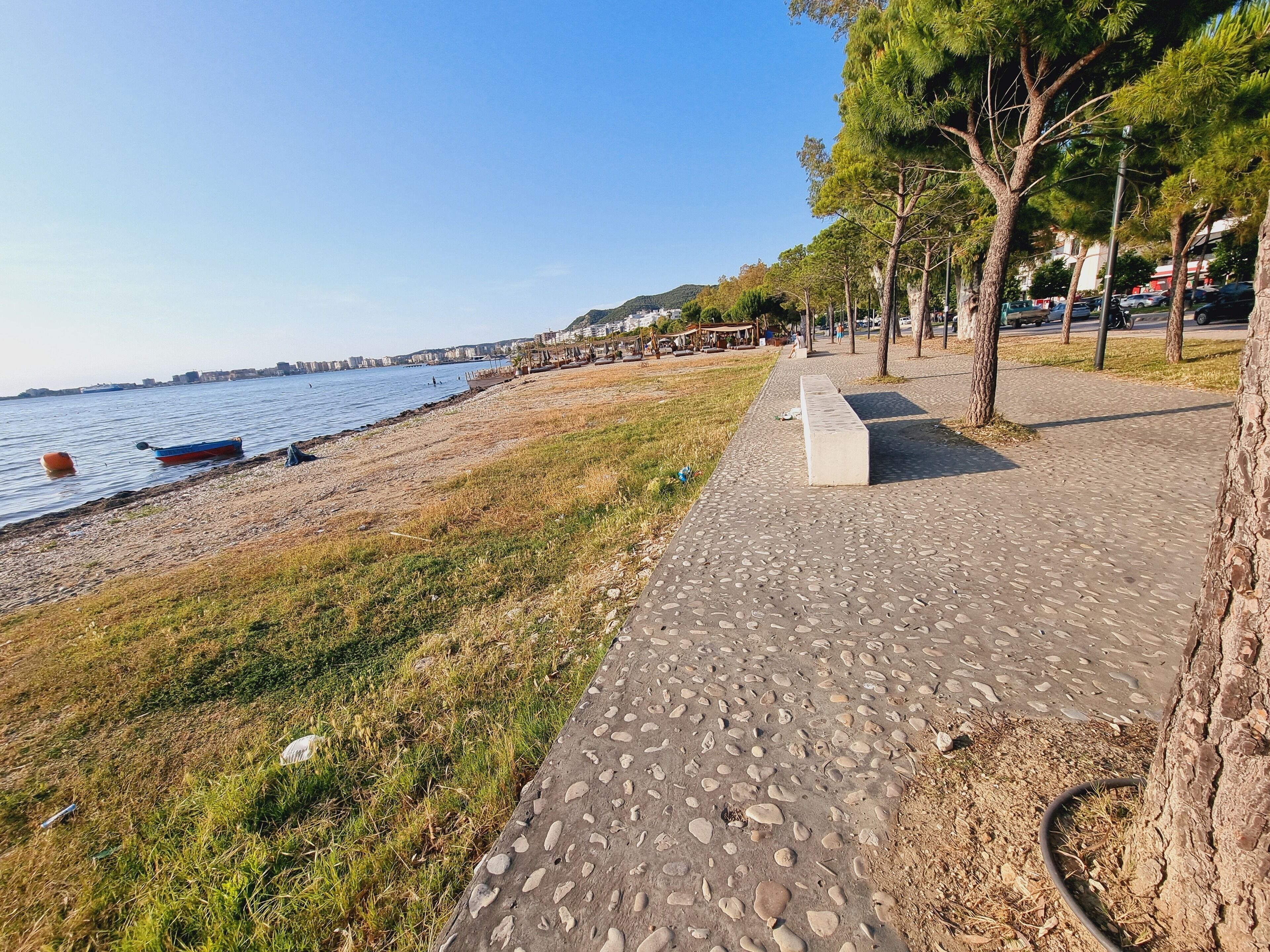 Ein Küstenweg mit Kiesweg, einer Bank und einer Rasenfläche direkt am Meer.