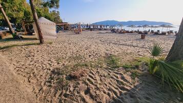 Une plage avec des tentes et des parasols, un ciel dégagé et des montagnes en arrière-plan.