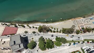 Vue aérienne d’une zone côtière comprenant un parking, un terrain de basketball et une plage avec des bateaux.