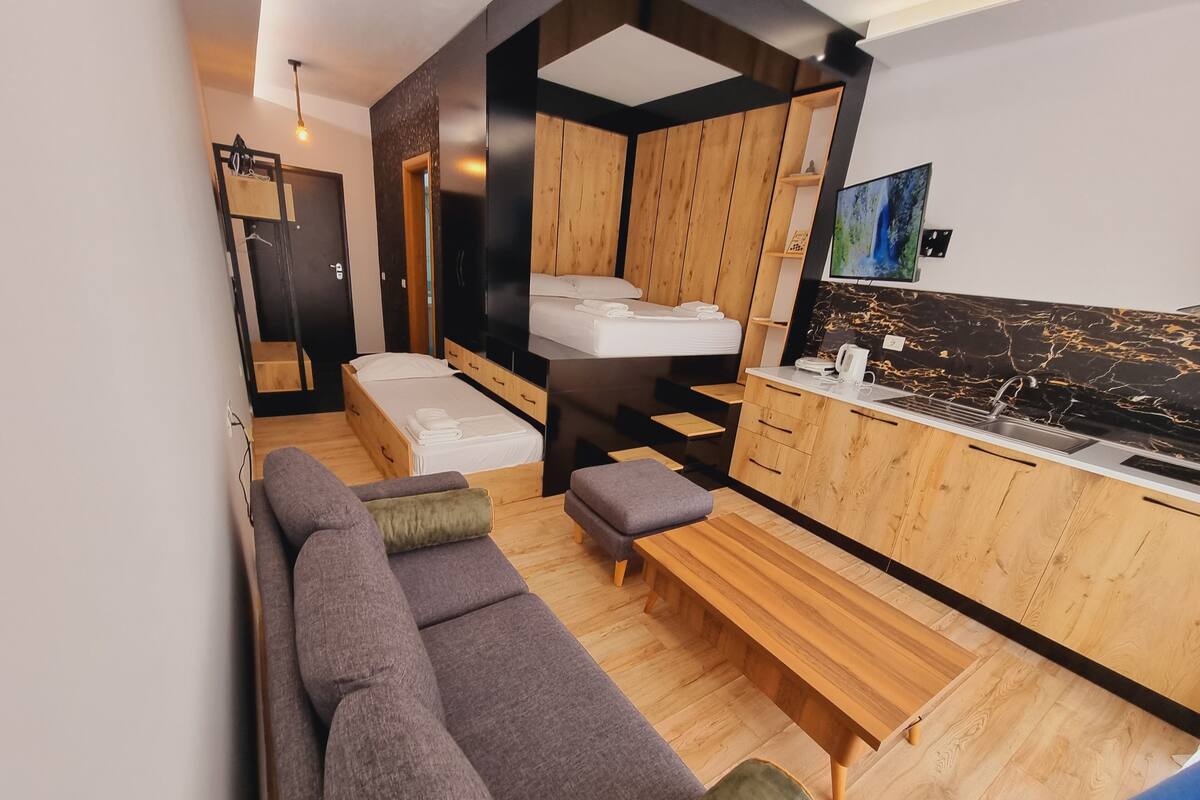 A modern, compact living space with a sofa, bench, and kitchenette.
