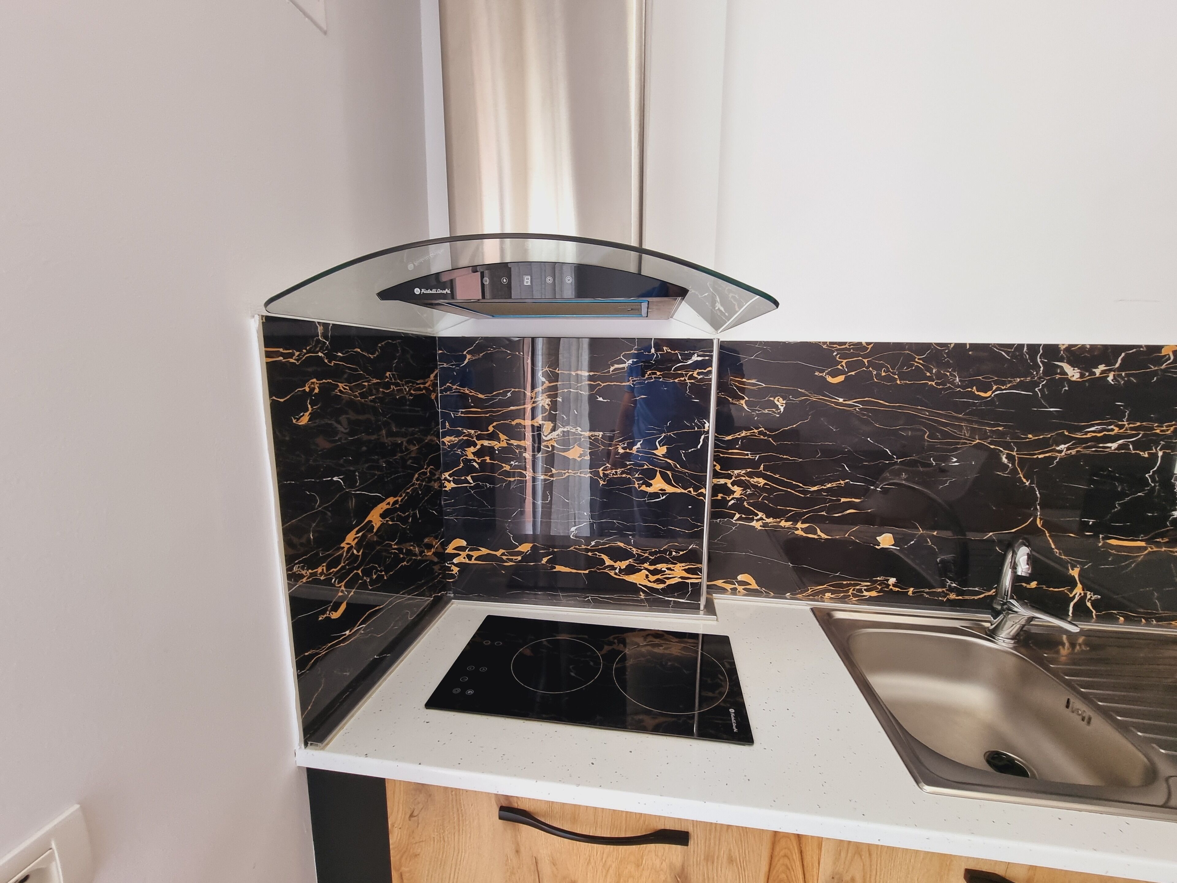 A kitchen with a black marble backsplash, a white countertop, a stainless steel sink, and a glass-enclosed stove.