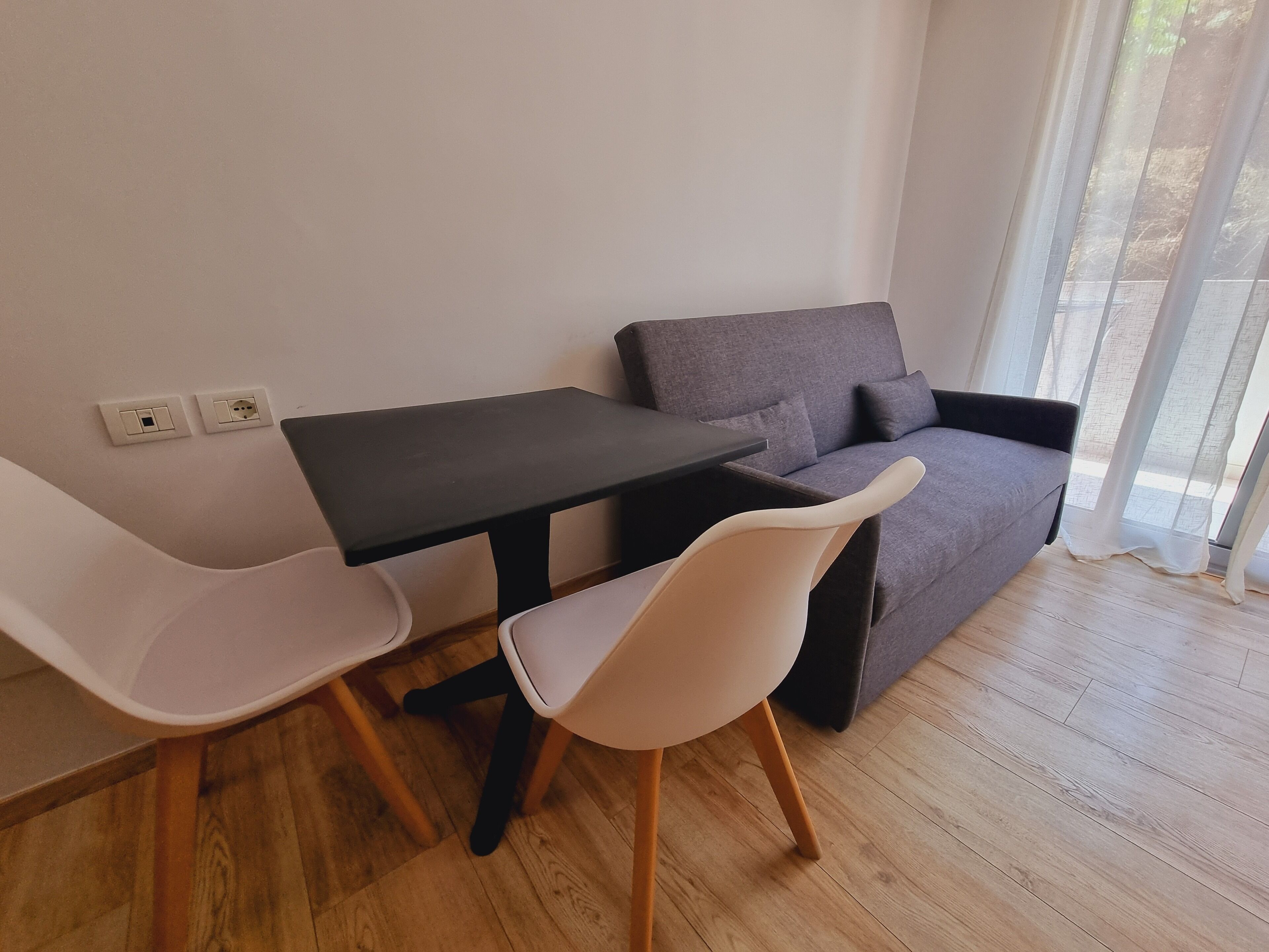 A modern living room with a grey sofa, a small black table, and two white chairs.