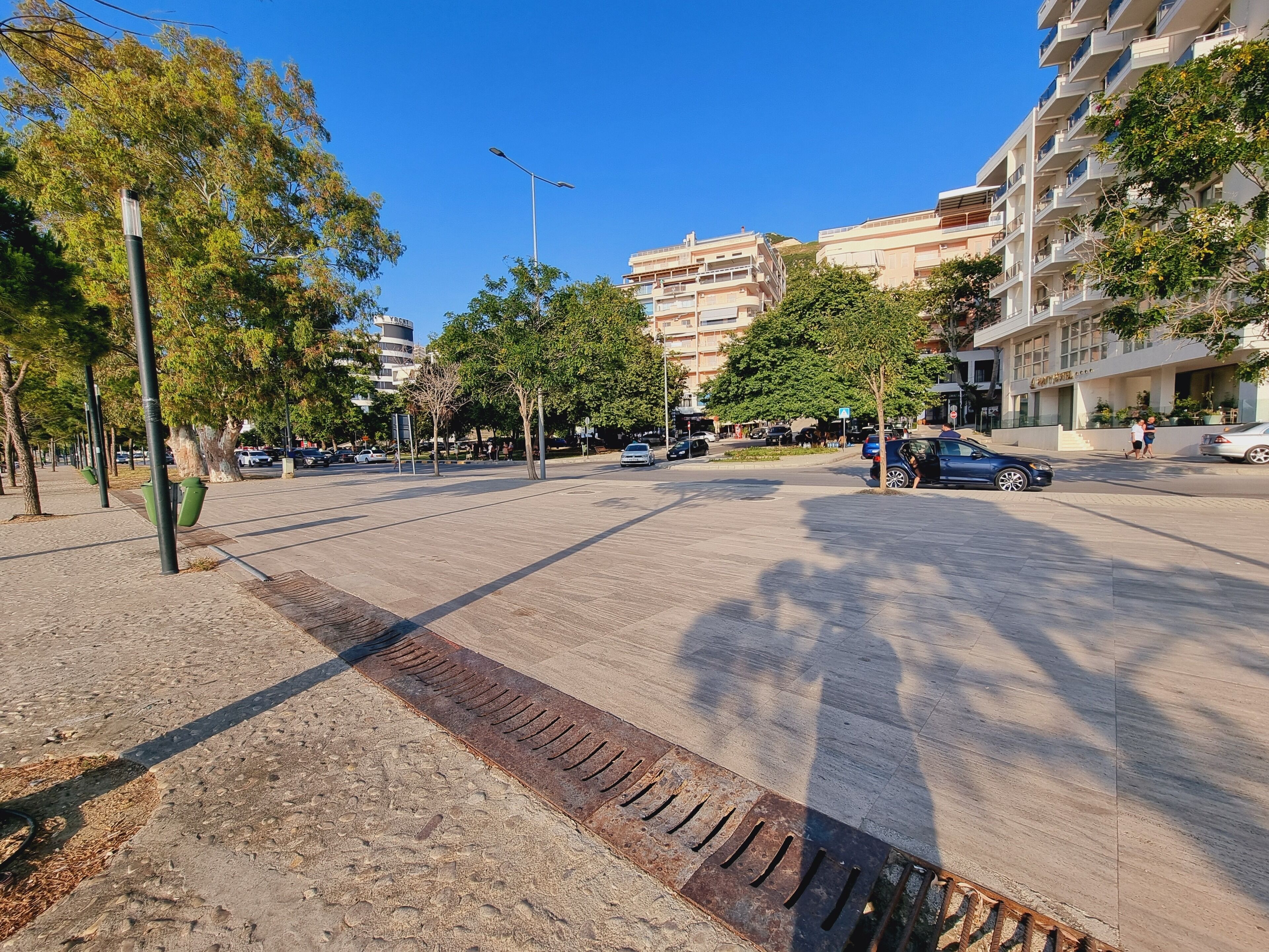 A spacious urban square with a central pedestrian area, surrounded by multi-story buildings with balconies and a café.