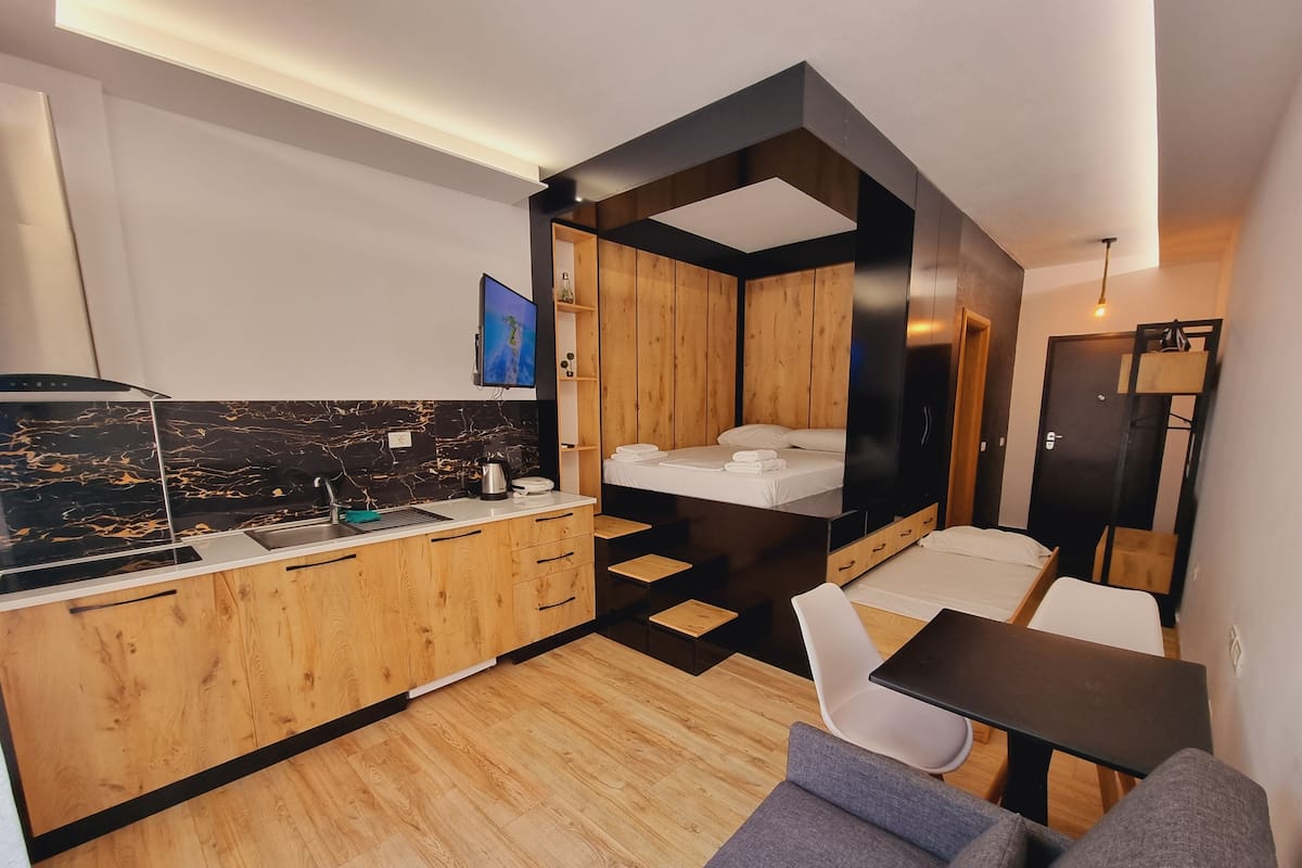 A compact, modern room with a kitchenette, a bed, a sofa, and a dining table.