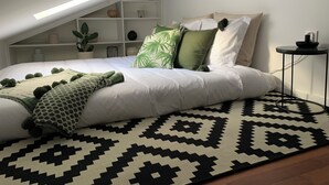 A bedroom with a sloped ceiling, a bed with white bedding, a patterned rug, and a small side table.