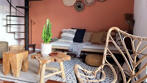 A cozy living room with a spiral staircase, a cactus plant, a woven chair, and a variety of decorative plates on the wall.
