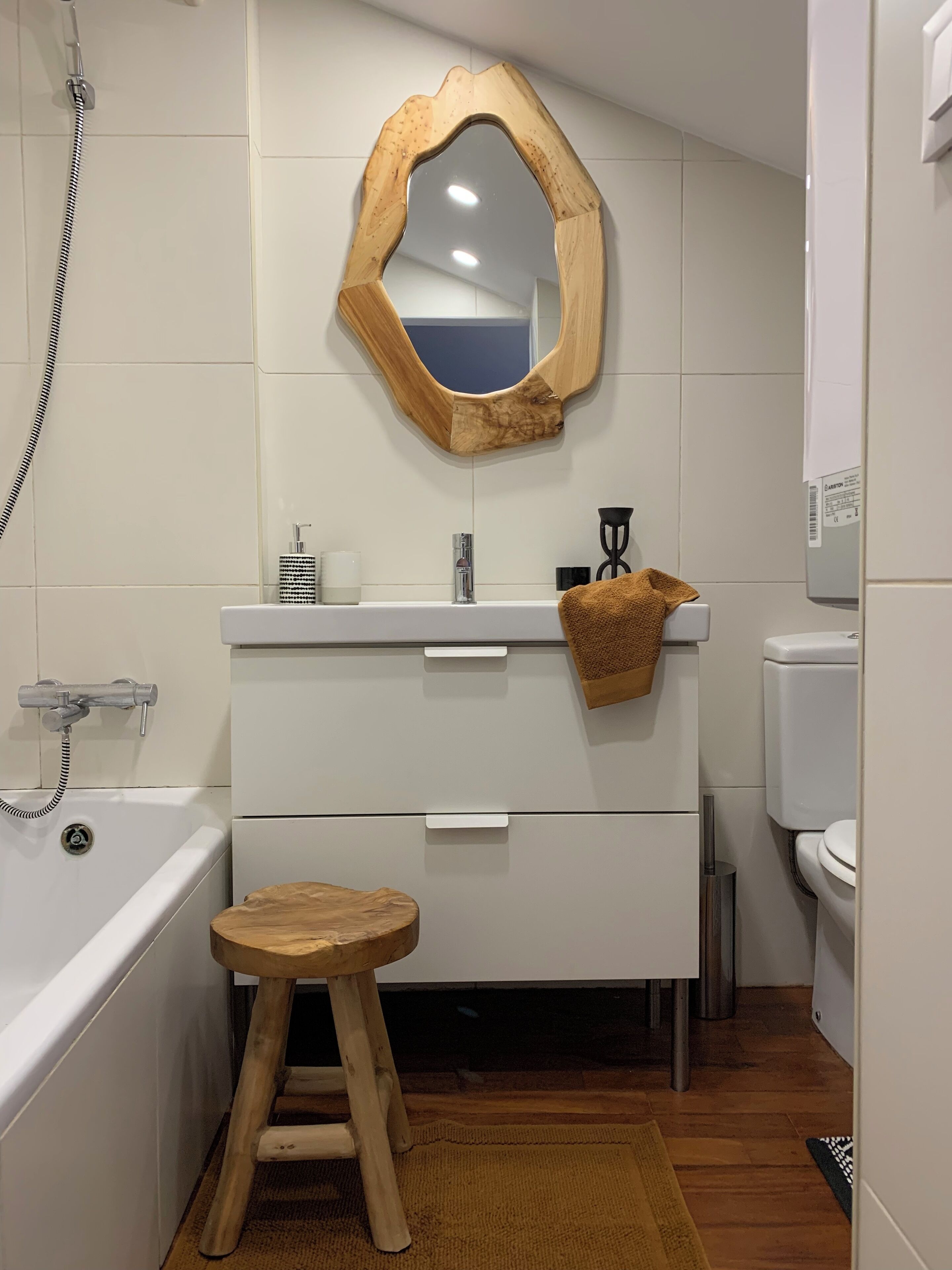 A bathroom with a wooden-framed mirror, a white sink, a wooden stool, a white toilet, and a bathtub.