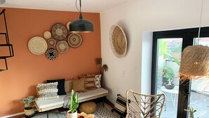 A cozy living room with a sofa, a wooden coffee table, and a wicker chair. There are various decorative items on the wall, including woven baskets and a hanging light fixture.