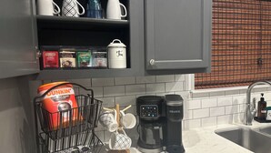 Una cocina con cafetera, hervidor y un espacio para colgar tazas.