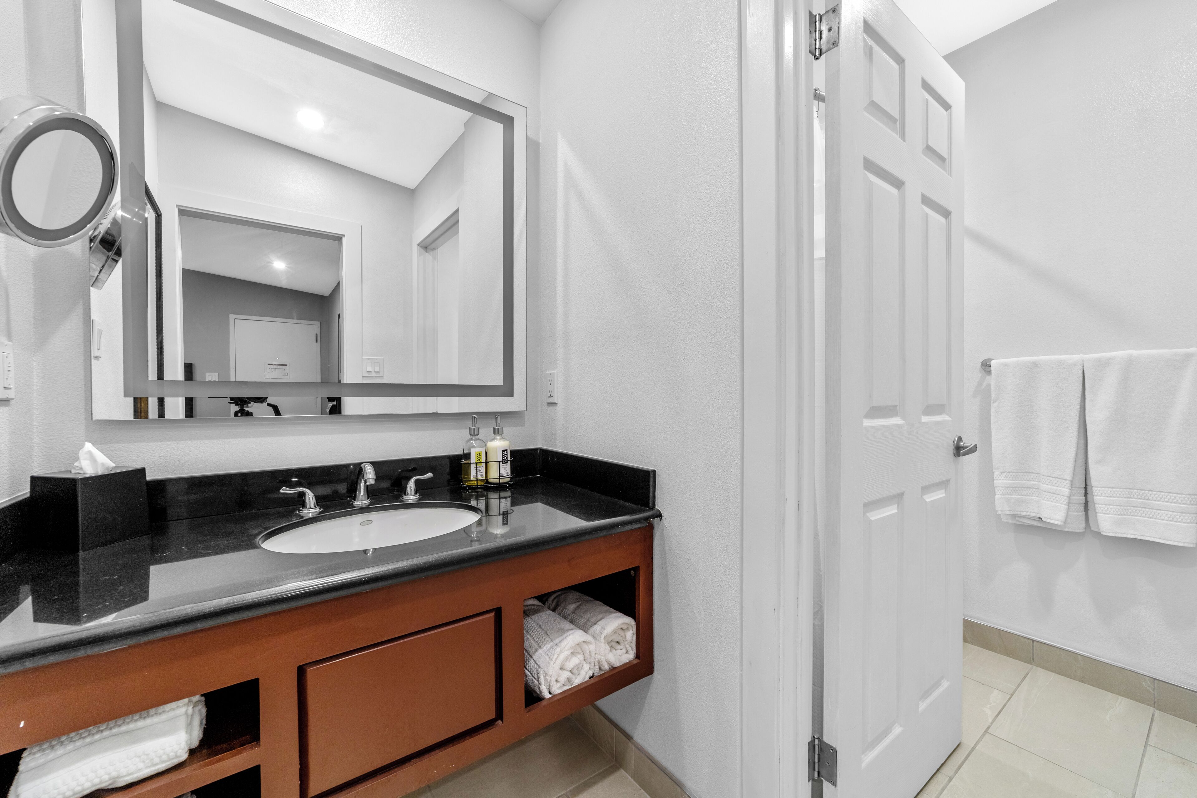 A modern bathroom with a black countertop sink, a large mirror, and a wooden vanity.