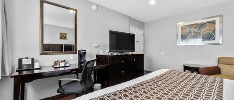 Habitación de hotel con cama, escritorio con computadora, televisor, cafetera y espejo.