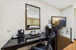 Habitación de hotel con escritorio, televisor, espejo, cafetera y un pequeño armario.