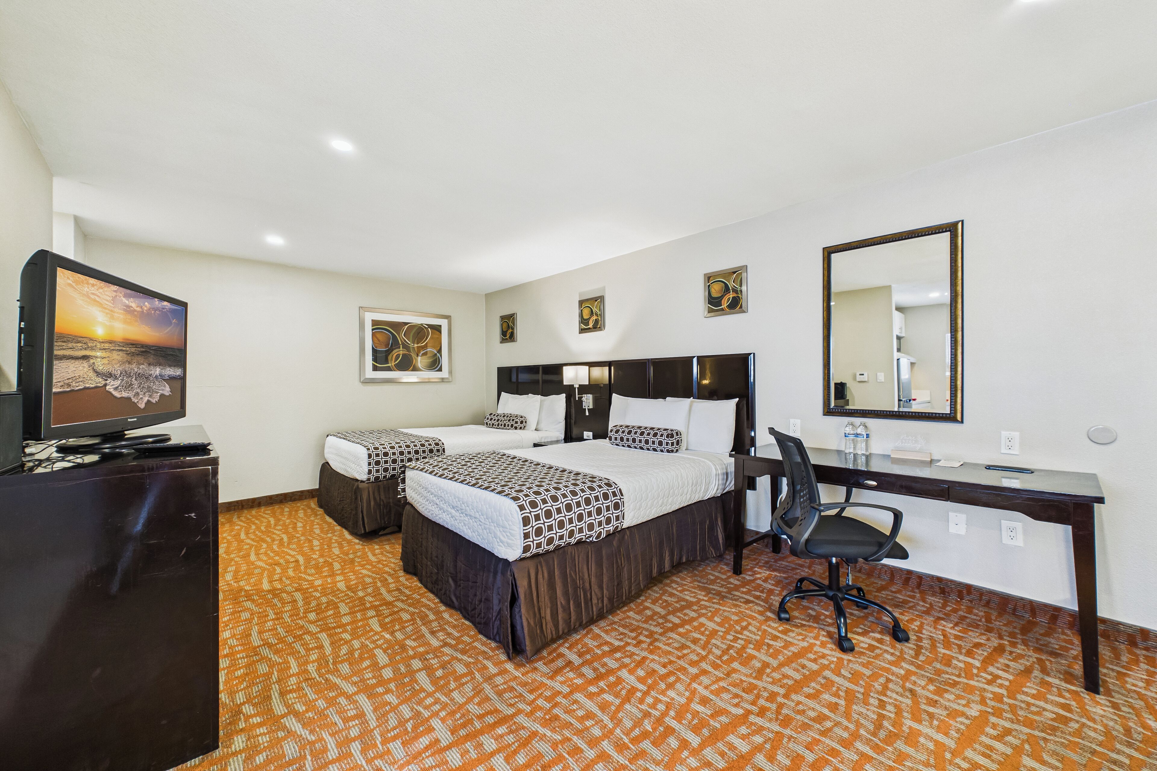 A hotel room with two beds, a desk, a chair, a television, and artwork on the walls.