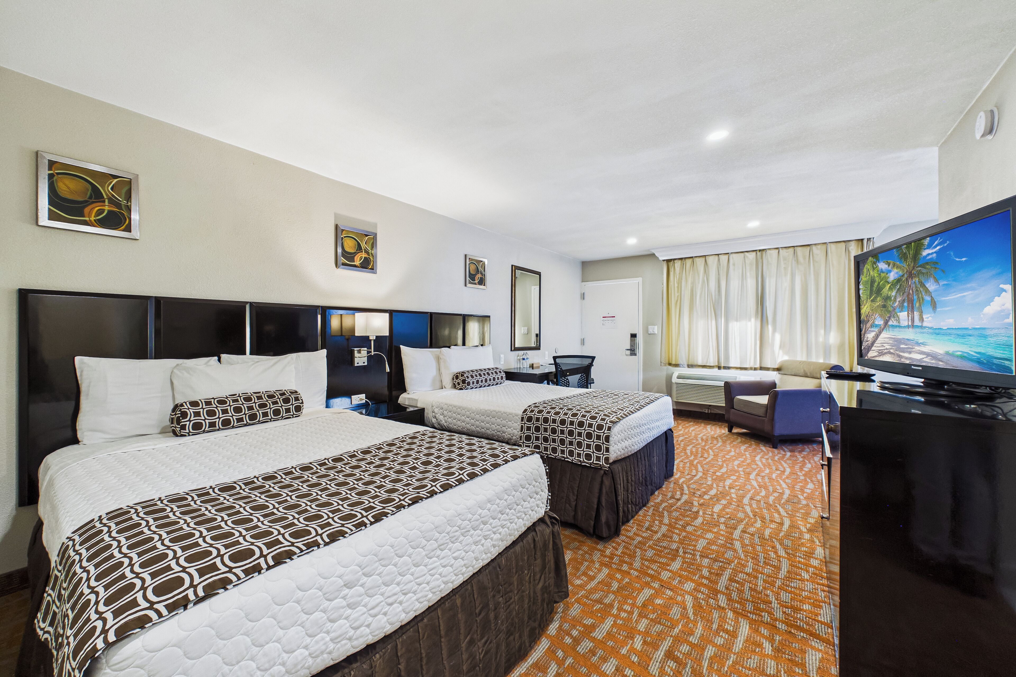 Habitación de hotel con dos camas, un escritorio, televisor y un ventanal con cortinas.
