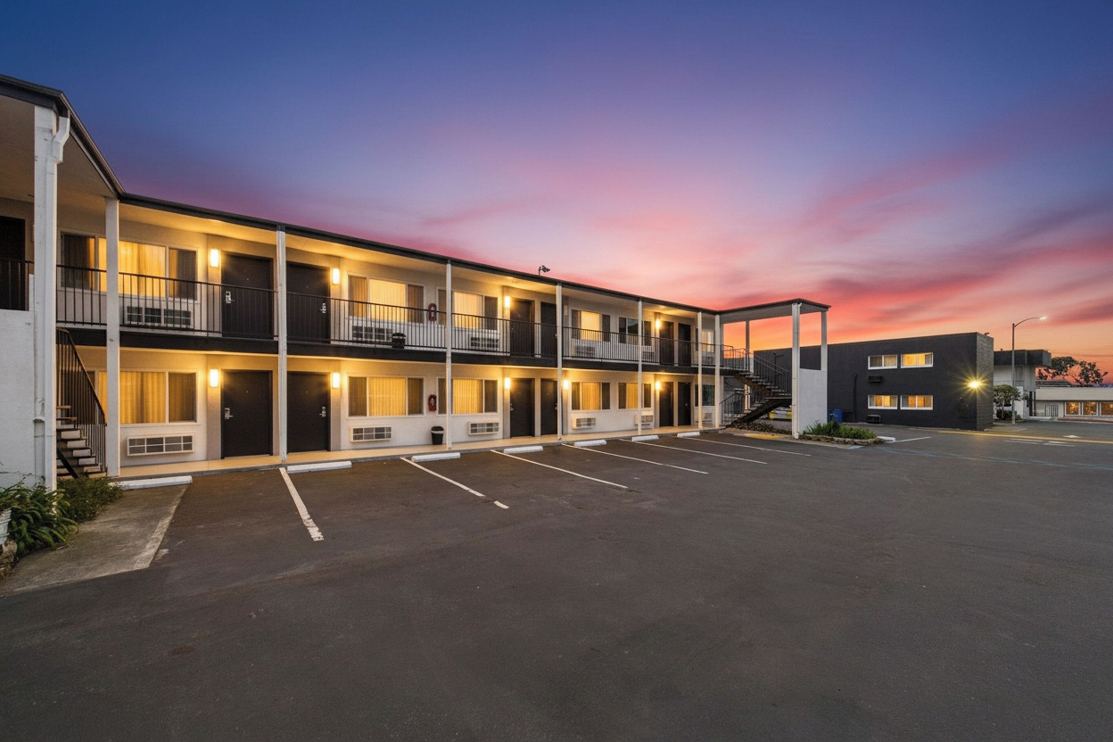 A multi-story motel with a parking lot, balconies, and a covered walkway.