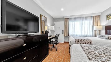 Habitación de hotel con una amplia televisión de pantalla plana, un escritorio con silla, dos camas con ropa de cama estampada y una ventana con cortinas.