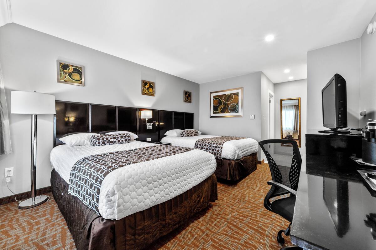 A hotel room with two beds, a desk, a chair, and a television.