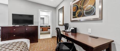 A hotel room with a bed, a desk, a chair, a television, a coffee maker, and a framed abstract painting on the wall.