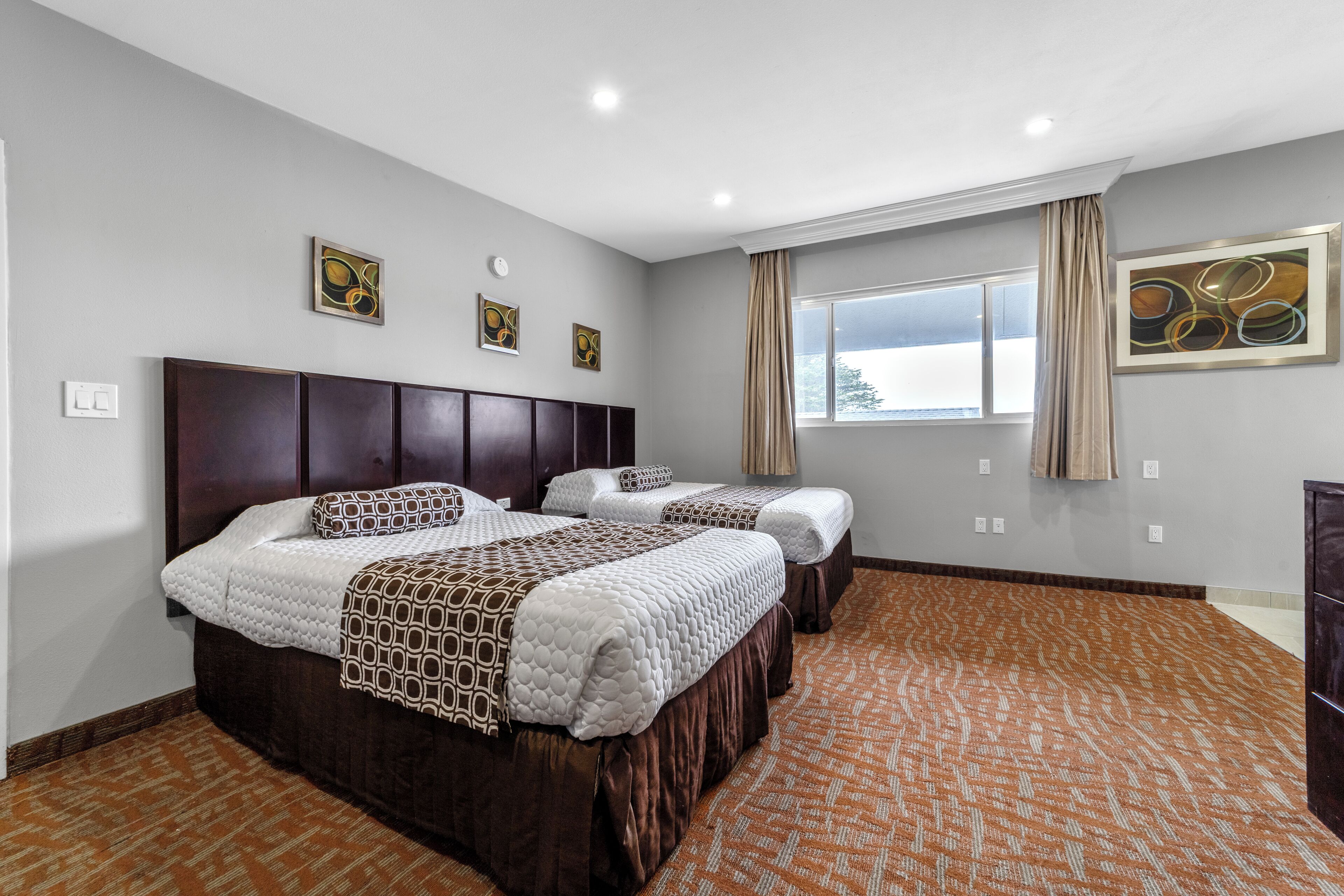 Une chambre d’hôtel avec deux lits, une grande fenêtre avec des rideaux et des œuvres d’art accrochées aux murs.
