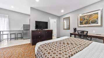 A hotel room with a bed, a desk, a chair, a television, and a kitchenette.